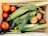 A wooden crate filled with fresh produce, including several ripe red tomatoes, ears of corn with husks, and a few peaches. Nestled among the vegetables is a small pepper. The arrangement showcases a variety of textures and natural colors.
