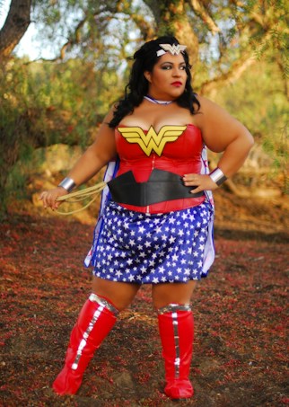 A person dressed in a Wonder Woman costume stands in a natural outdoor setting. The outfit includes a red bodice with a yellow emblem, blue skirt with white stars, and red boots. The person wears a tiara and holds a golden lasso.
