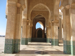 Arched stone structures with ornate green tile patterns on the lower sections create a symmetrical and grand architectural design. The flooring also features intricate geometric patterns. Natural light filters through the arches, highlighting the textures and colors.