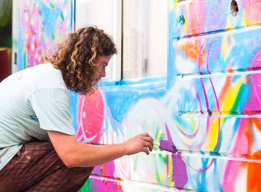 a man painting a wall with colorful graffiti