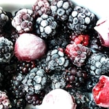 A close-up view of a variety of frozen berries, primarily consisting of blackberries and raspberries, with a light frost covering them.