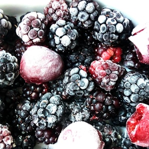 A close-up view of a variety of frozen berries, primarily consisting of blackberries and raspberries, with a light frost covering them.