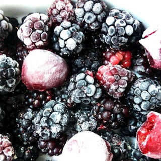 A close-up view of a variety of frozen berries, primarily consisting of blackberries and raspberries, with a light frost covering them.