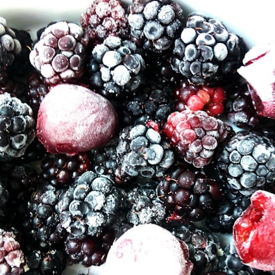 A close-up view of a variety of frozen berries, primarily consisting of blackberries and raspberries, with a light frost covering them.