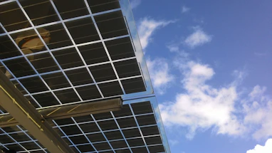 A panoramic view of a solar panel field under a bright blue sky at sunrise.