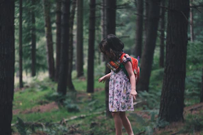 girl walking in field surrounded with tall and green trees