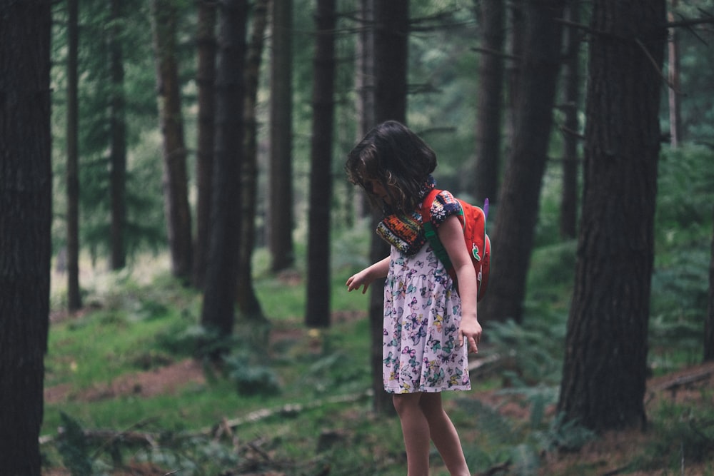 girl walking in field surrounded with tall and green trees