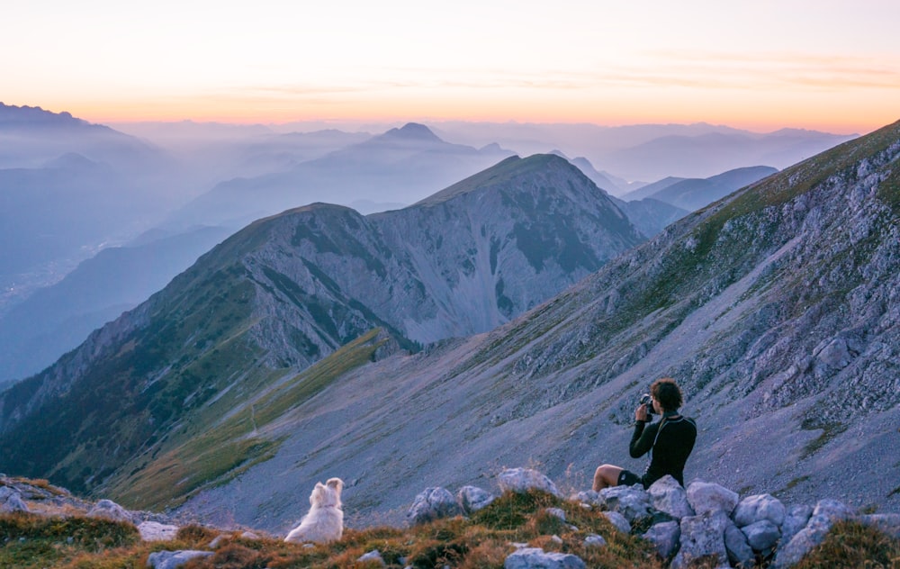 person sitting on mountain near white dog during daytime