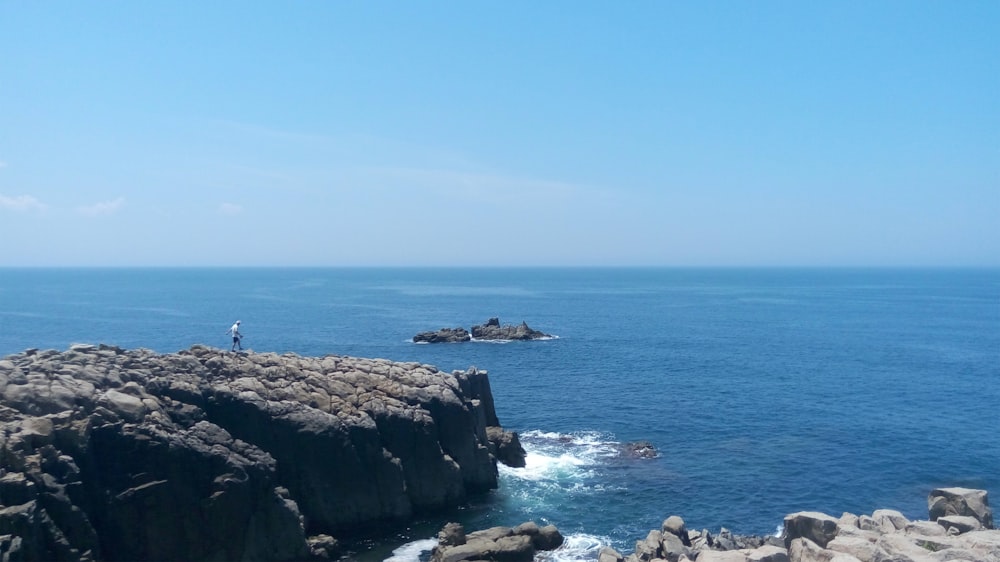 personne debout au sommet d’une formation de pierre grise près de la mer pendant la journée