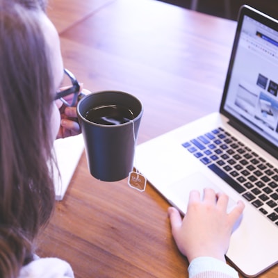 woman holding tea filled mug using MacBook