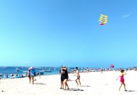 Children playing on a sunny beach with colorful kites flying overhead.