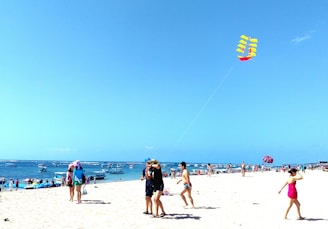Children playing on a sunny beach with colorful kites flying overhead.