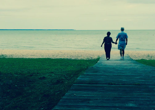 A cinematic photo of a couple walking hand in hand along a sandy path with charcoal shadows.