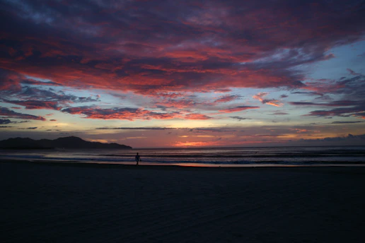 A vibrant sunset over a serene beach, with a solo female traveler soaking in the moment.