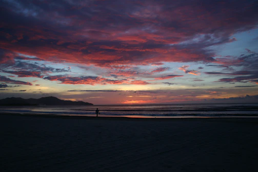 A vibrant sunset over a serene beach with a lone traveler capturing the moment.