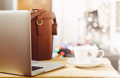 An overhead view of a chic workspace with a sleek laptop, soft pink notebook, and a cup of herbal tea.