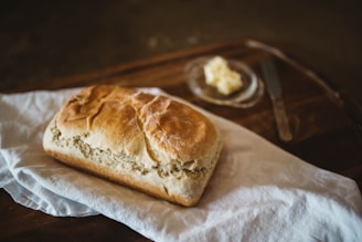 A warm loaf of bread on a wooden table surrounded by fresh ingredients.