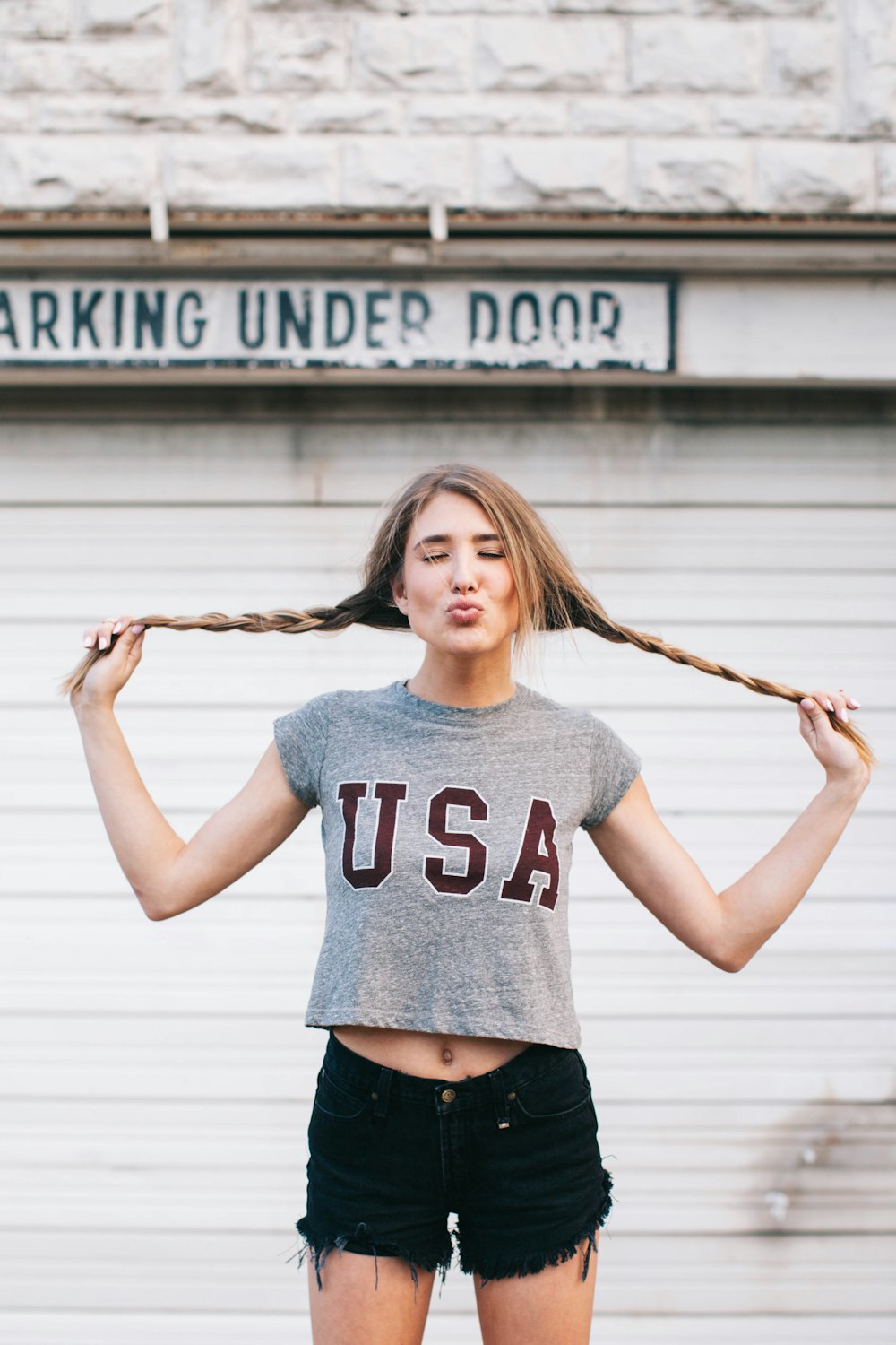 standing woman holding her pig tail tied hair pouting her lips in front of building