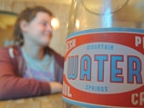 A close-up of a vintage-style bottle label for 'Mountain Springs Water' is in focus, while a person in casual attire is blurred in the background.