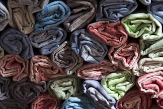 Rows of rolled up fabric are neatly stacked, showcasing a variety of colors including blue, red, green, and beige. The fabric appears to have a textured, striped pattern, and is arranged tightly with careful precision.