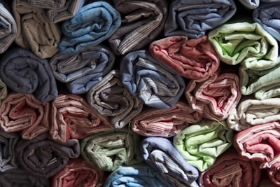 Rows of rolled up fabric are neatly stacked, showcasing a variety of colors including blue, red, green, and beige. The fabric appears to have a textured, striped pattern, and is arranged tightly with careful precision.