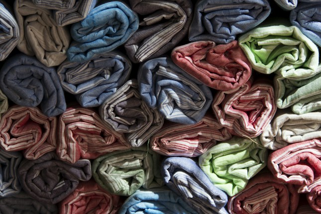 Rows of rolled up fabric are neatly stacked, showcasing a variety of colors including blue, red, green, and beige. The fabric appears to have a textured, striped pattern, and is arranged tightly with careful precision.