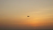 A discreet helicopter hovering over Cartagena’s coastline under a muted sunset.