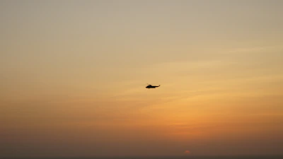 A discreet helicopter hovering over Cartagena’s coastline under a muted sunset.
