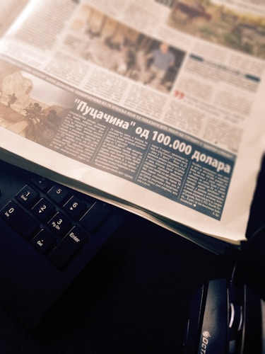 A newspaper page with an article featuring a photograph and text in a foreign language. The page is placed atop a black computer keyboard, with headphones partially visible on the side.