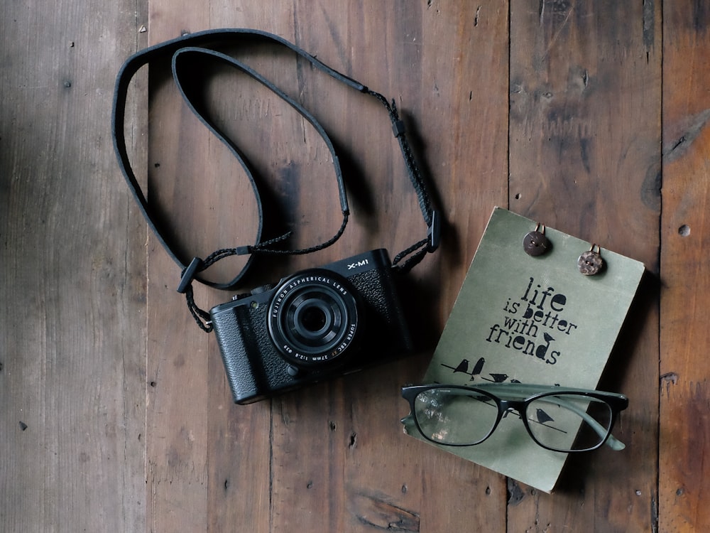 photographie à plat de l’appareil photo MILC noir et des lunettes sur une table brune