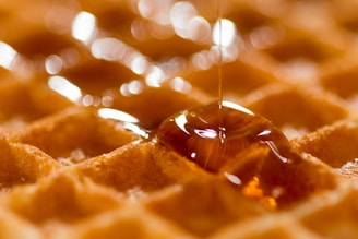 A close-up of a golden syrup pouring from a glass jar onto a wooden surface.