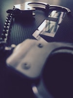 A pair of black leather cuffs with metal buckles resting on a smooth dark surface with subtle reflections.