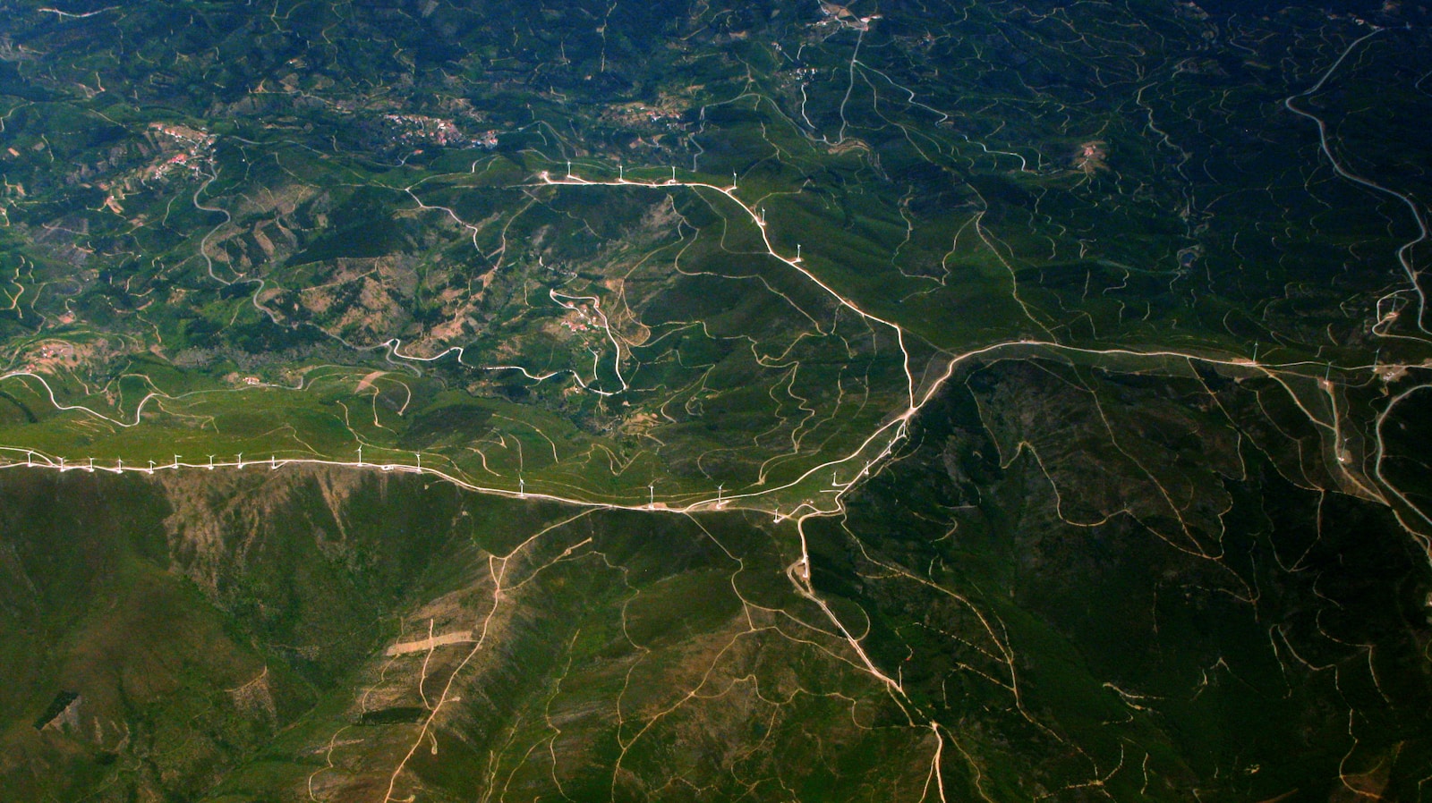 An aerial view of pale roads winding across densely green hills