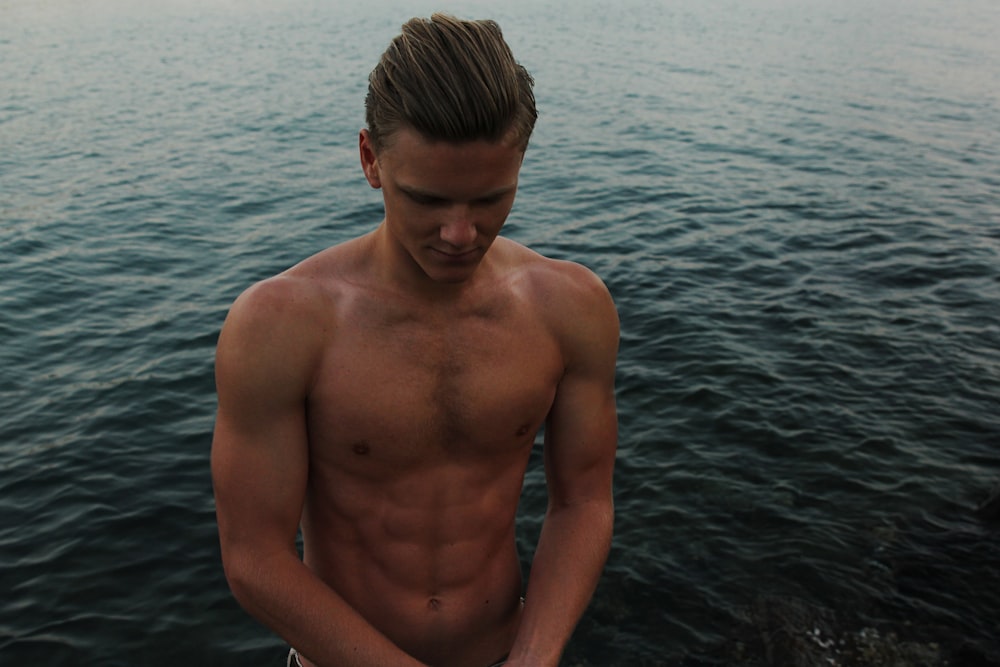 topless man looking down with ocean background