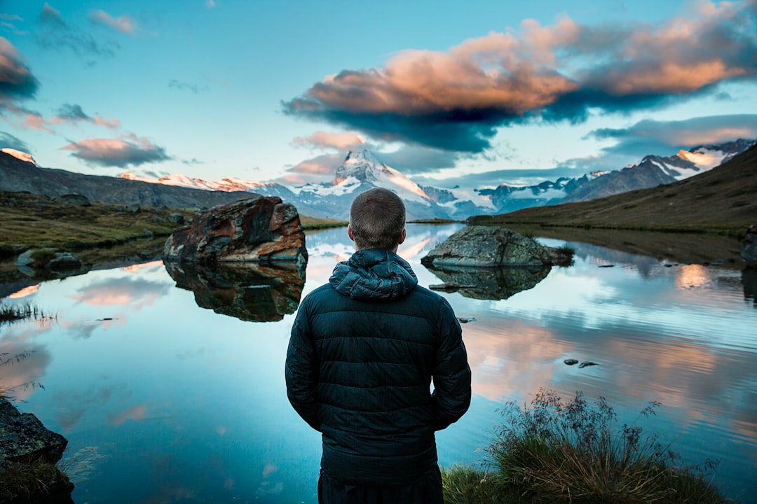 man standing in front view of lake surrounded with mountains