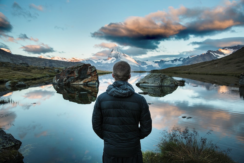 man standing in front view of lake surrounded with mountains