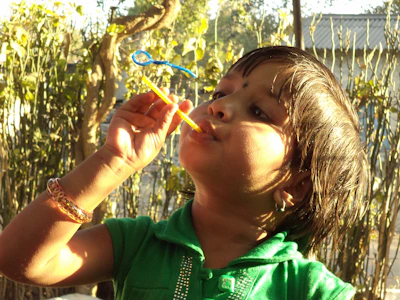 A joyful child blowing bubbles with friends, sunlight sparkling through the bubbles.