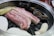 A sizzling grill filled with raw slices of pork belly meat, mushrooms, and shellfish. The food items are arranged neatly on a circular grill, with a small brown ceramic pot in the background. The pinkish hue of the pork contrasts with the earthy tones of the mushrooms and shellfish.