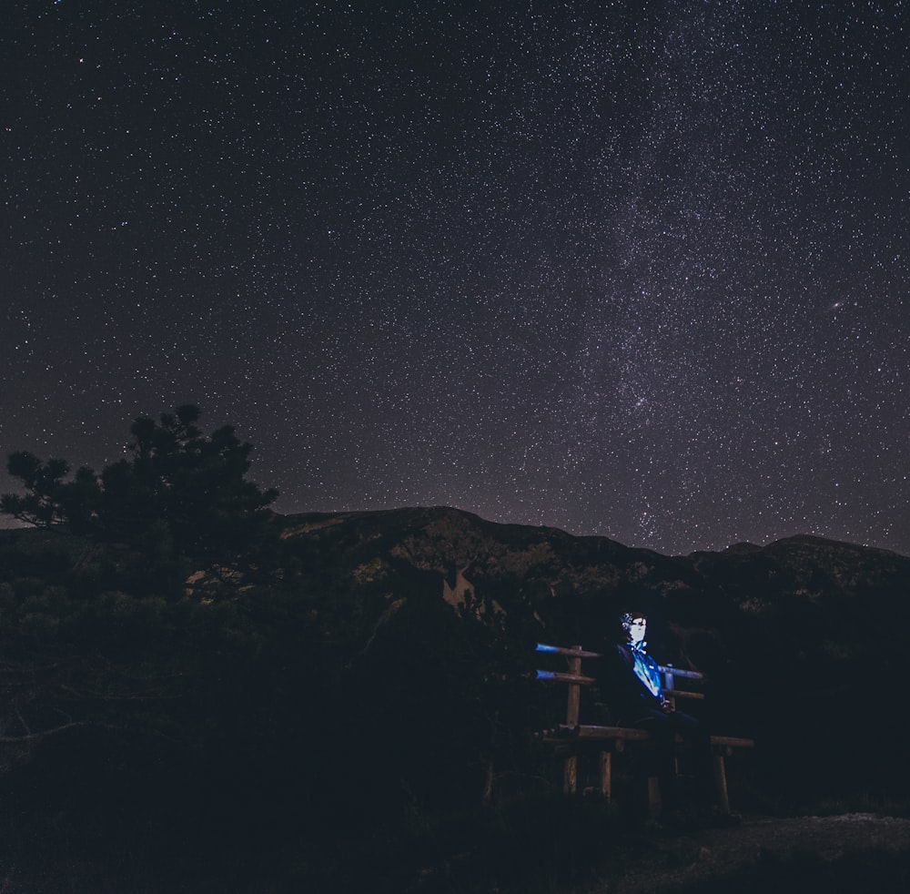 a person sitting on a bench under a night sky