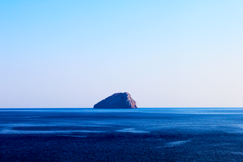 islet on body of water under cumulus clouds