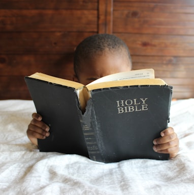 boy reading Holy Bible while lying on bed