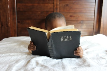 boy reading Holy Bible while lying on bed