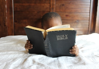 boy reading Holy Bible while lying on bed