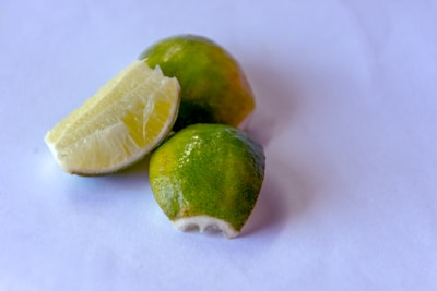 A few pieces of lime, with one piece cut open to reveal the juicy interior, placed on a plain white background.