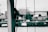A close-up view of ropes tied around a vertical pole with a blurred background featuring some buildings and nature. The image is tinted in monochromatic green tones, giving it an abstract and artistic feel.