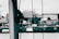 A close-up view of ropes tied around a vertical pole with a blurred background featuring some buildings and nature. The image is tinted in monochromatic green tones, giving it an abstract and artistic feel.