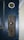 A rusty metal door lock and keyhole plate on a painted wooden door. The lock is old and has visible signs of wear and corrosion. Above the plate, there is a brass deadbolt lock.