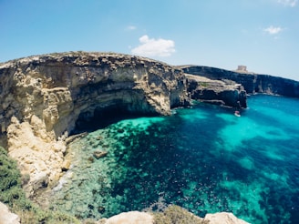 A close-up of an ocean rowing boat slicing through turquoise coastal waters under a clear sky.