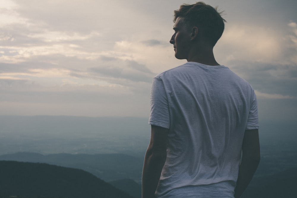 man standing facing mountains during sunset