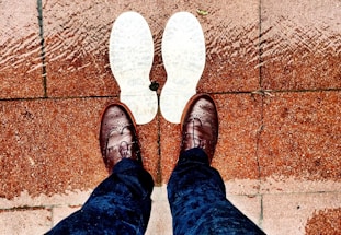 Brown brogue shoes on a wet sidewalk with a distinctive shadow or worn outline of white shoe soles on the ground.